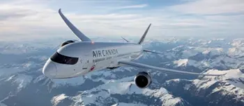 Air Canada airplane flying high in the sky above snow-covered mountains on a clear day.