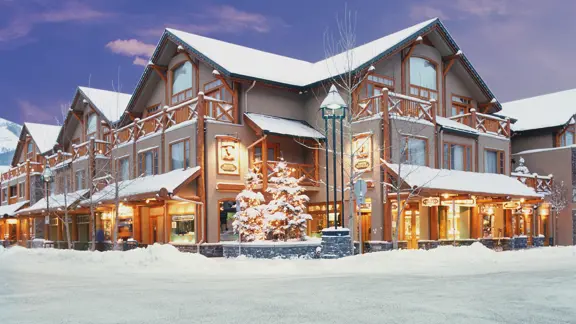 The exterior of the hotel, covered in snow with warm light coming through the windows and a clear sky.