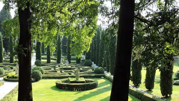 Scenic view of Giardino Giusti in Italy, featuring manicured Renaissance-style hedges, cypress trees, and classical statues.