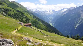 Panoramic view of the Ahorn Mountain in Mayrhofen, Austria, featuring snow-capped peaks, green alpine meadows, and a clear blue sky.