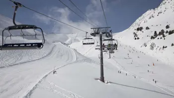 A ski lift carries a group up along a mountainside, allowing them to enjoy the surrounding views of vast snowy slopes and clear blue skies.