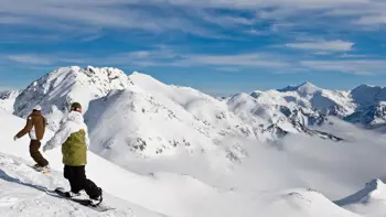 A couple slide their way along a snowy slope in Arinsal, surrounded by views of vast white mountains and clear blue skies.