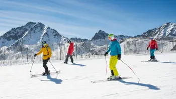 A group of skiers glide their way down a slope, surrounded by panoramic views of snowy mountains.