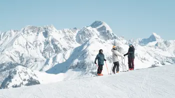 A group stand atop a snowy peak, looking out into the surrounding mountains and valleys.