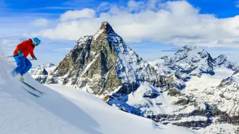 A lone skier rushes down a piste in Zermatt, kicking up powdered snow as they take in the nearby mountains and snowy valleys.