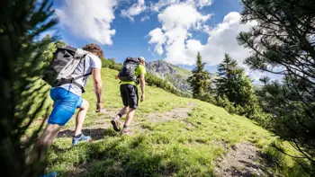 Couple walking uphill through lush green terrain in St. Anton, surrounded by vibrant vegetation and scenic hillside views.