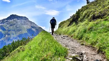 Hiker walking up a scenic trail in the Neustift mountains, surrounded by rocky peaks and alpine meadows under a blue sky