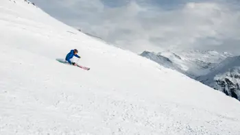 A lone skier rushes down a slope in Davos, kicking up powdered snow as they descend.