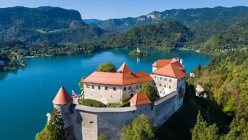 Aerial view of Bled Castle overlooking Lake Bled, with the island church and surrounding green hills.